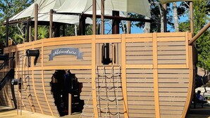 Une structure de jeu en bois, portant l’inscription « Aventure », et comprenant un filet d’escalade et un toboggan.