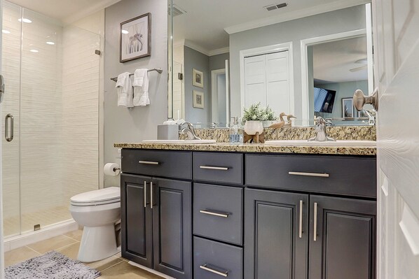 A bathroom with a shower, toilet, dark cabinets, a sink with a mirror, and a towel rack. - Lush villa with on site pool, WiFi, private washer dryer & central AC (Hilton Head)