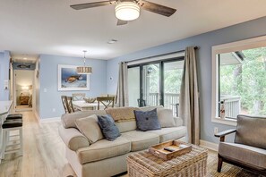 A living room with a sofa, a coffee table, a ceiling fan, and a large window with curtains. - Lush villa with on site pool, WiFi, private washer dryer & central AC (Hilton Head)