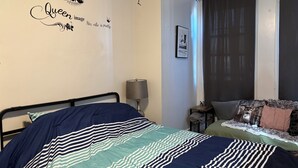 A bedroom with a bed, a wall decoration, a lamp, a window with curtains, and a small table. -  1-bedroom Temple near train and buses (Philadelphia)