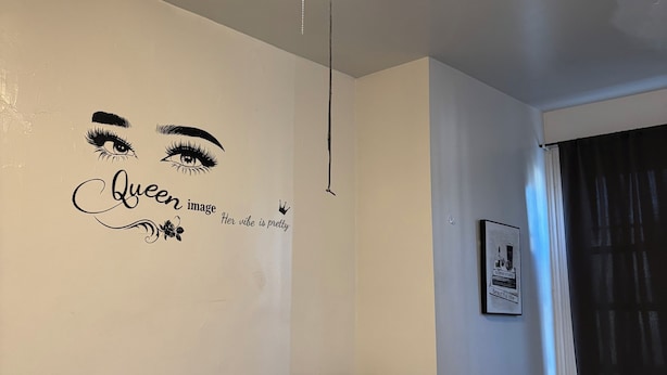 A bedroom with a bed, a ceiling fan, a wall with a decorative image, a bedside lamp, and a window with curtains. -  1-bedroom Temple near train and buses (Philadelphia)