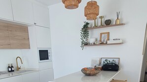 Una cucina moderna con mobili bianchi, un'isola centrale con piano di lavoro bianco, sedie in legno e lampade a sospensione in fibra naturale.