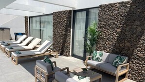 Un'area lounge all'aperto illuminata dal sole, con poltrone, un divano e un tavolino da caffè.