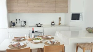 Una cucina moderna con mobili bianchi, forno a microonde integrato e un'area pranzo con sedie di legno e tovaglia a quadretti.