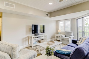 A living room with a television, white furniture, a sofa, and a window. - Dreamy Villa island getaway with pool,tennis & balcony (Hilton Head)