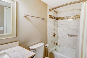 Une salle de bain comprenant des toilettes, un lavabo et une baignoire, le tout recouvert de carreaux imitant le marbre.