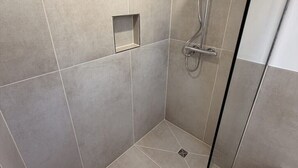 Un espace douche doté d’une porte en verre, de murs carrelés et d’un pommeau de douche en métal.