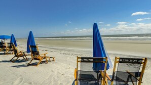 Sedie a sdraio e ombrelloni su una spiaggia sabbiosa, con cielo sereno.