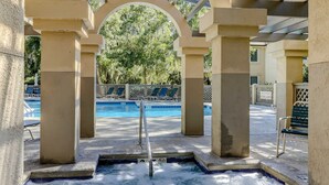 Area piscina con vasca idromassaggio, poltrone relax e zona salotto coperta.