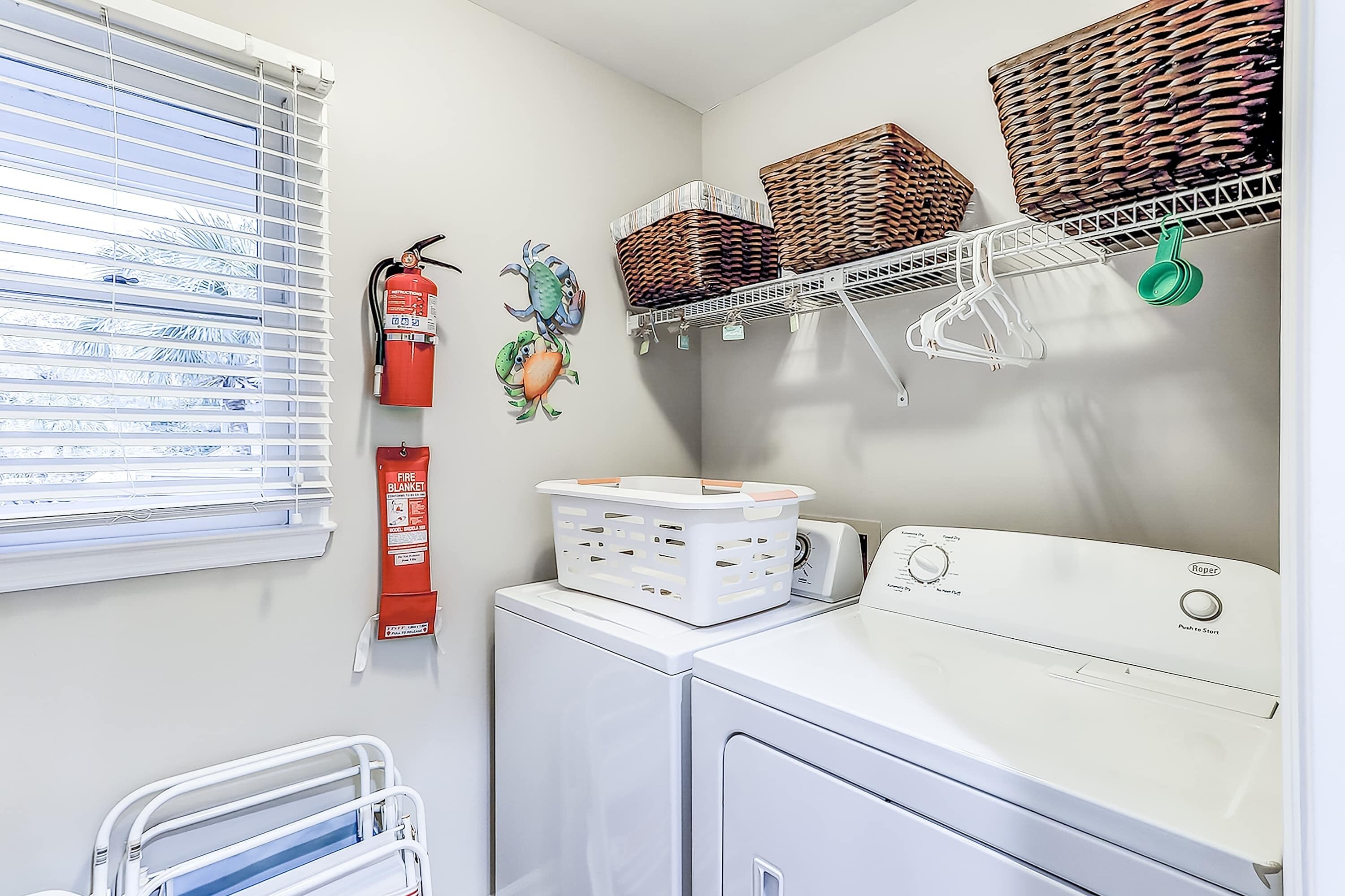 A laundry area with a washing machine, drying rack, baskets, and a fire extinguisher.