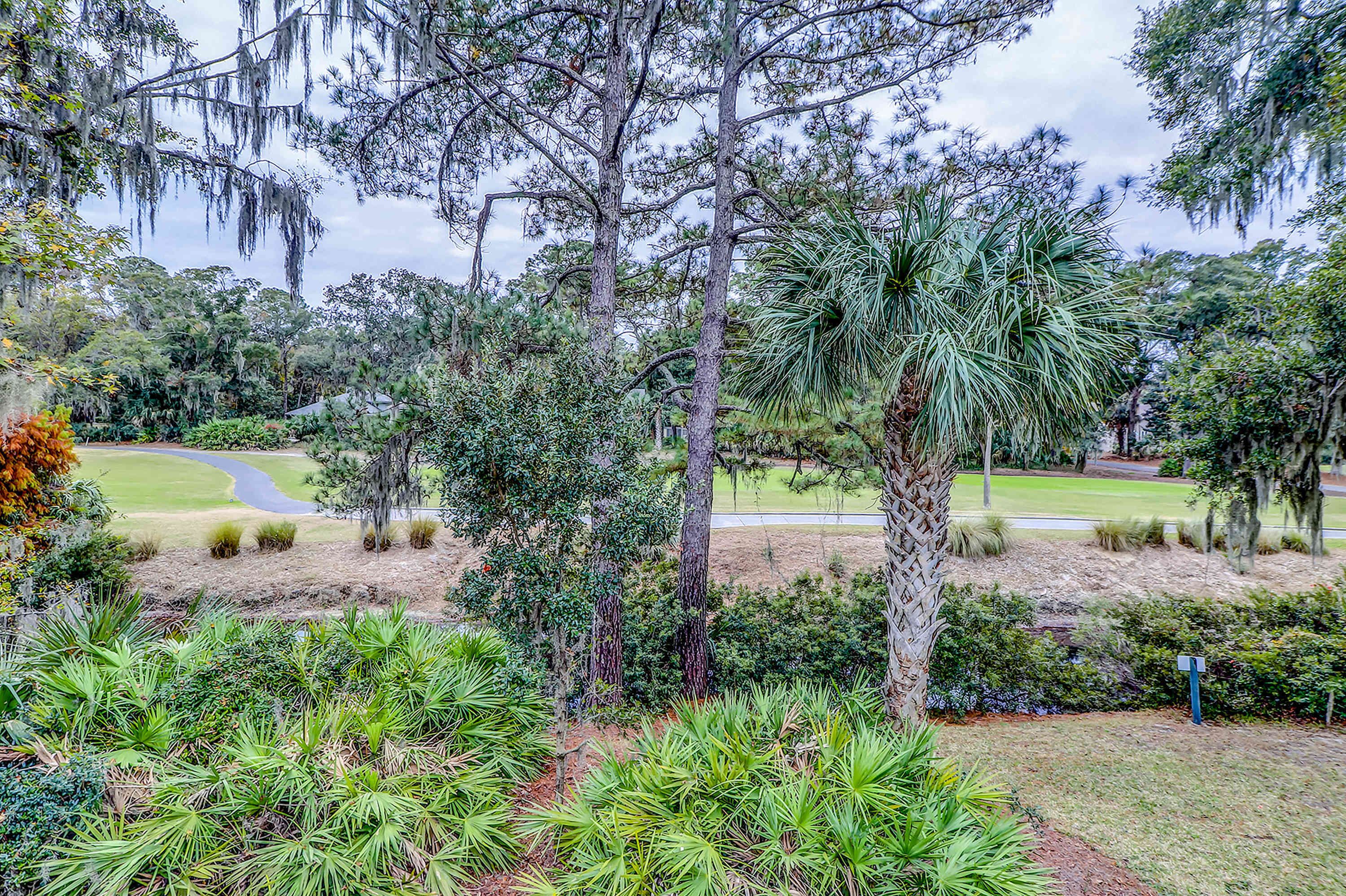 A landscaped garden with various trees and shrubs, a winding path, and a golf course in the background.