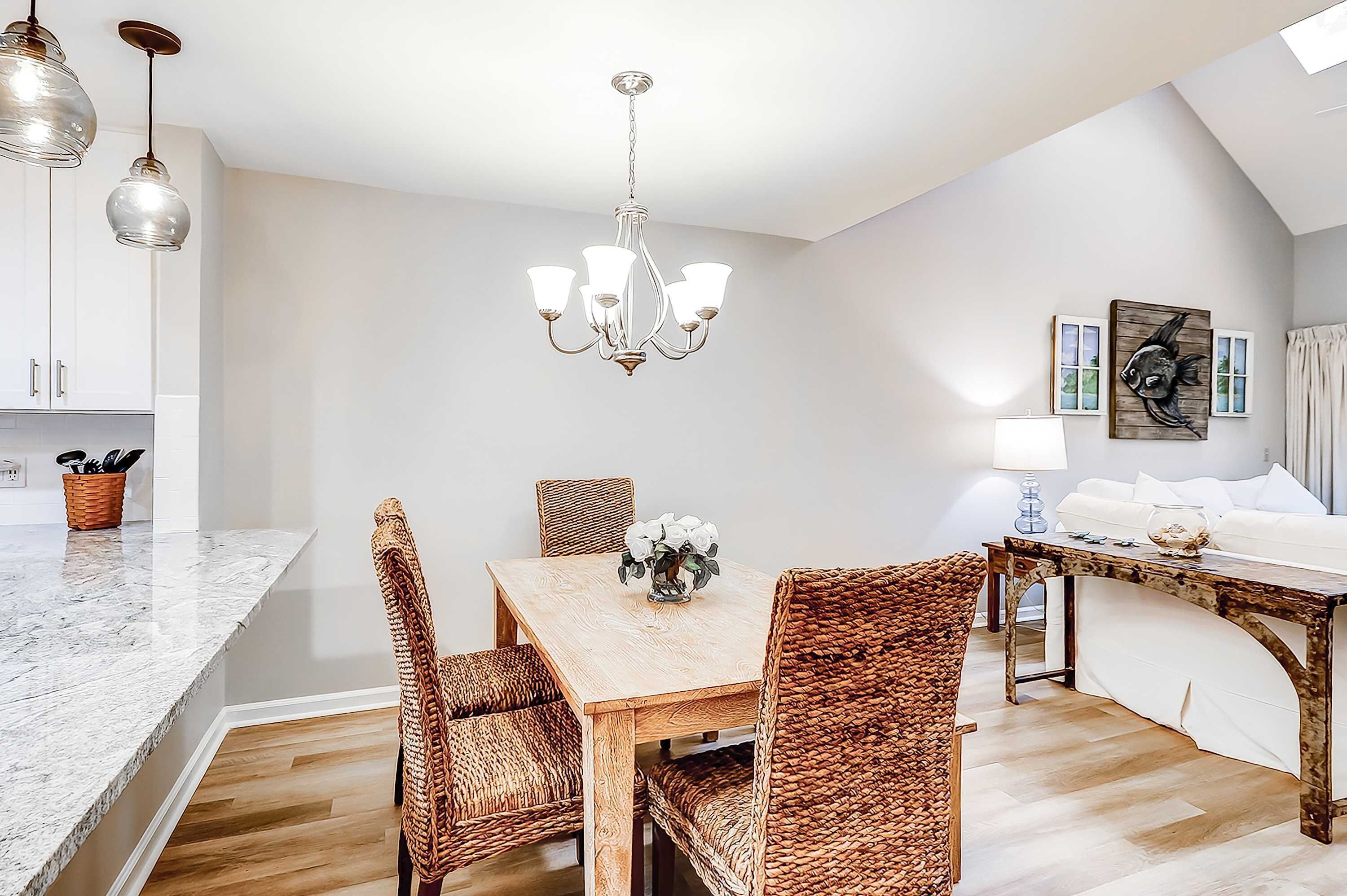 Een eetgedeelte met een houten tafel, rieten stoelen, een kroonluchter en uitzicht op de keuken.