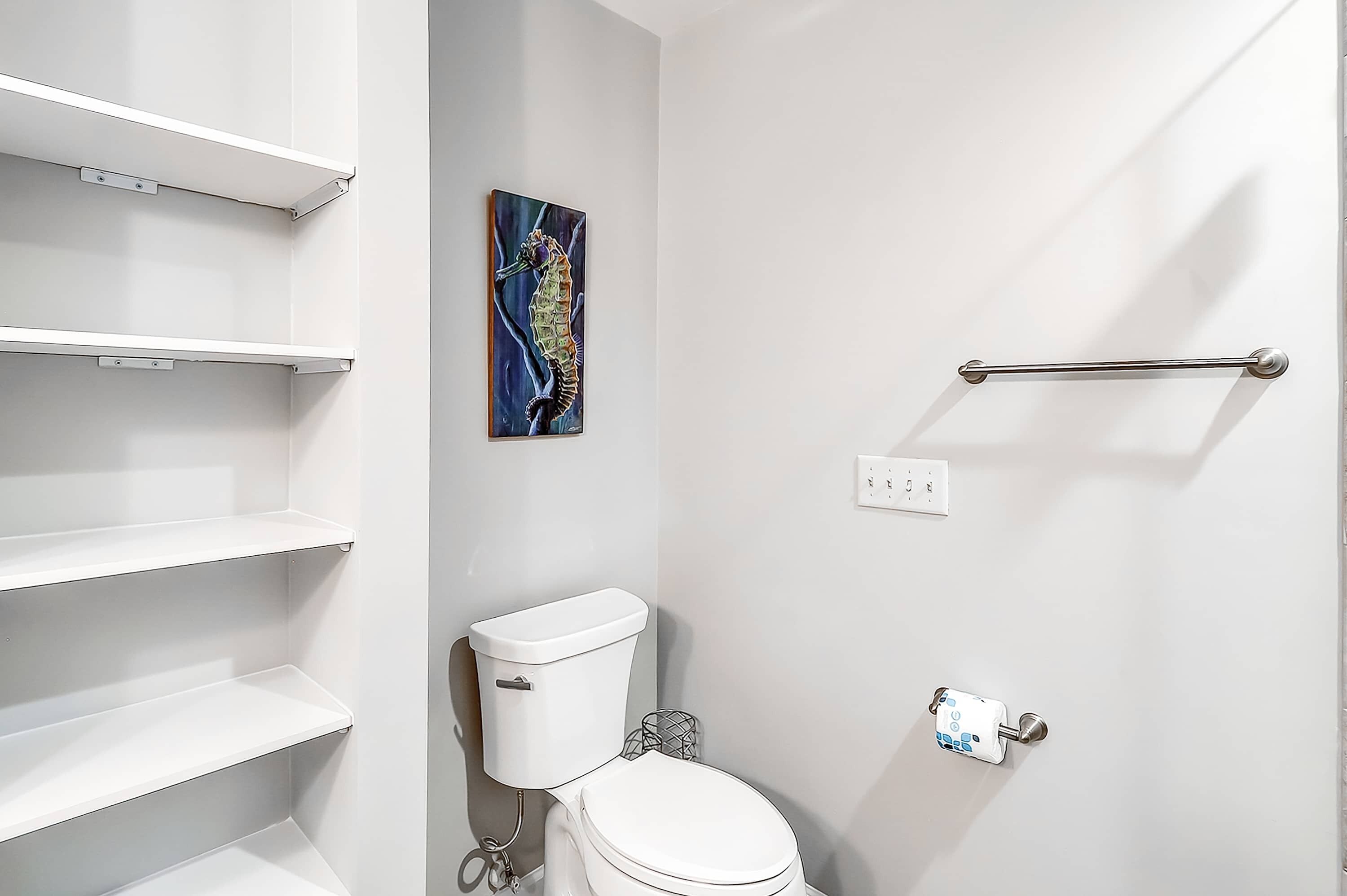 Une salle de bain avec des murs blancs, des toilettes, une barre d’appui, un porte-serviettes et une étagère.