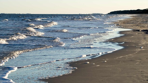 En strand med bølger, sand og en fjerntliggende kystlinje.