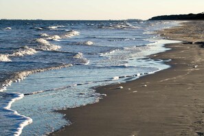 A beach with waves, a sandy shore, and a distant shoreline. - 2-bedroom beachside condo with balcony, pools, & WiFi - near golf & beach (Hilton Head)