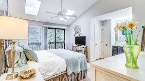 A bedroom with a bed, bedside table, lamp, TV, and a green vase with flowers. - Dog Friendly Villa with Walkable Beach Access, AC, Deck, WiFi & Shared Pool (Hilton Head)
