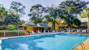 A swimming pool with lounge chairs, a small building with a red door, and surrounding trees. - Dog Friendly Villa with Walkable Beach Access, AC, Deck, WiFi & Shared Pool (Hilton Head)