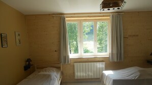 Una habitación con dos camas, una ventana con cortinas, un radiador y una lámpara sobre una mesita de noche.