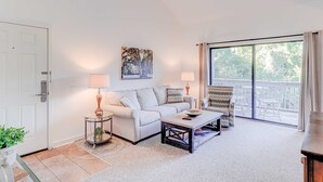 A living room with a sofa, armchair, coffee table, and a painting on the wall. - Snowbird Friendly villa with Golf View, Patio, Shared Pool, Tennis, AC, WiFi (Hilton Head)