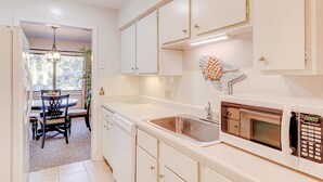 A kitchen with white cabinets, a stainless steel sink, a microwave, and a dining area with a table and chairs. - Snowbird Friendly villa with Golf View, Patio, Shared Pool, Tennis, AC, WiFi (Hilton Head)