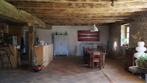A rustic interior with a wooden ceiling, a dining area with a table and chairs, a kitchen with a refrigerator, and a large abstract painting on the wall.