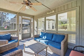 Una habitación soleada con muebles de mimbre, ventilador de techo y ventanas amplias.