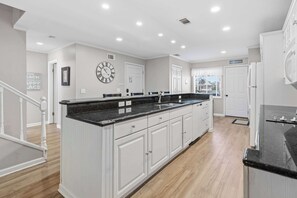 A modern kitchen with white cabinetry, a black countertop, and a large island. - Updated all-suite tennis villa with W/D, pool, screened porch - near beach (Hilton Head)