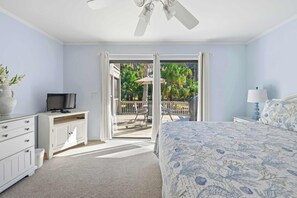 A bedroom with a bed, a TV, a dresser, and a balcony with outdoor furniture. - Updated all-suite tennis villa with W/D, pool, screened porch - near beach (Hilton Head)
