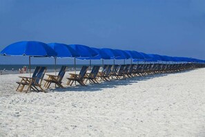 Ein Strand mit blauen Sonnenschirmen und Holzliegen.