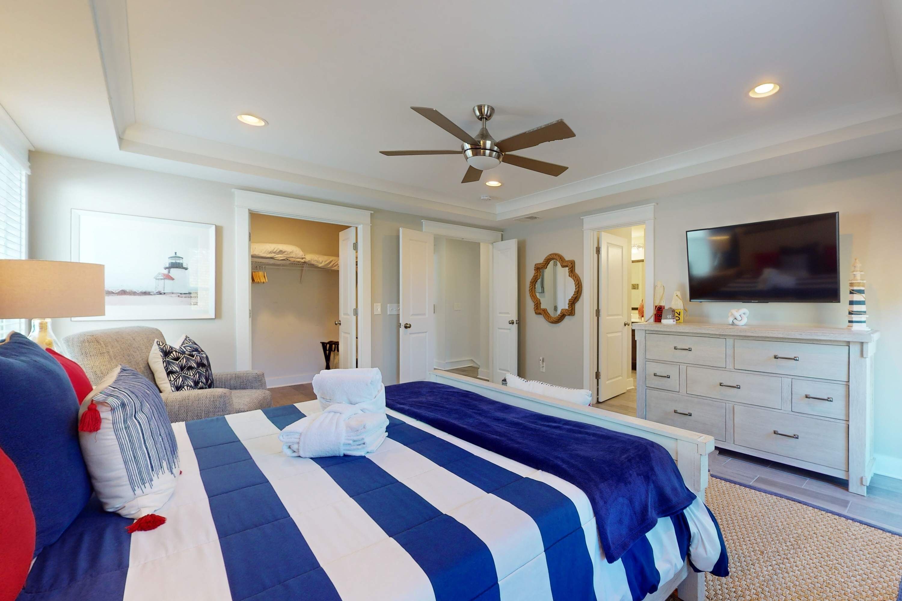 A bedroom with a bed, a ceiling fan, a TV, a dresser, and a door leading to another room.