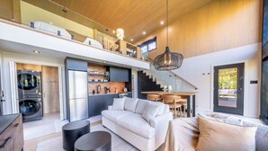 Una cocina moderna con horno empotrado, un área de comedor con mesa y sillas, un sofá y una escalera que conduce a un nivel superior.