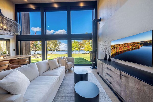 Ein modernes Wohnzimmer mit großem Fernseher, einer Couch und Blick auf einen See.