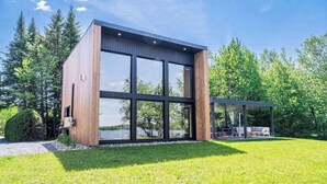 Un edificio moderno de dos pisos con amplios ventanales, una zona de estar exterior cubierta y vistas a un lago.