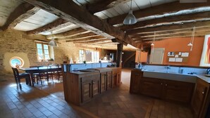 Une cuisine spacieuse avec des poutres en bois, un grand îlot central et un coin repas doté d’une table ronde.