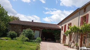 Un bâtiment rustique avec un toit en tuiles, un chemin de gravier et un espace jardin agrémenté de plantes en pot.