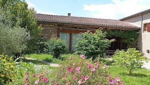 Una casa de piedra rústica con tejado de tejas, rodeada por un jardín con diversas plantas en flor.