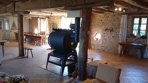 Un intérieur rustique avec des poutres apparentes, des murs en pierre, un grand radiateur industriel et un coin repas doté de meubles en bois.
