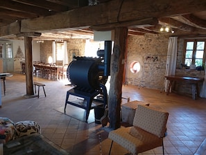 A rustic interior with exposed wooden beams, stone walls, a large industrial heater, and a dining area with wooden furniture. - Spacious 12-Person Country House in the Tarn Countryside (Andouque)
