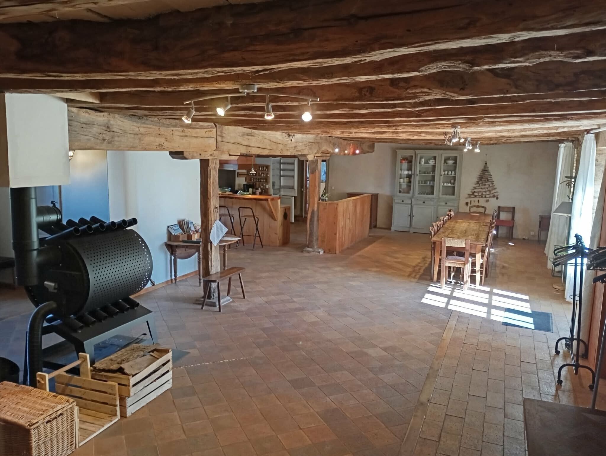 Une cuisine rustique avec un poêle à bois, un coin repas doté d’une longue table et un îlot de cuisine.