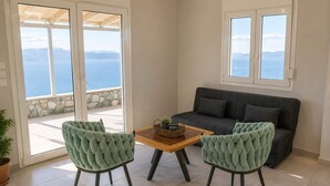 A room with a sofa, two chairs, a table, and a view of the sea through a glass door.
