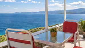 A covered outdoor seating area with a table and chairs, overlooking a body of water and distant mountains.