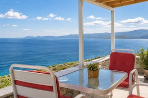 A covered outdoor seating area with a table and chairs, overlooking a body of water and distant mountains.