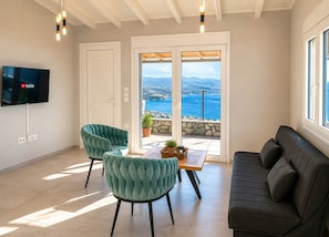 A living room with a TV, two chairs, a sofa, and a balcony with a view.