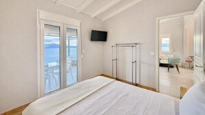 A bedroom with a bed, a TV, a balcony with chairs, and a view of the sea.