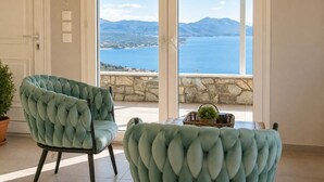 A room with a view of the sea and mountains, featuring two plush armchairs and a small table with a plant.