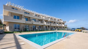 A multi-story hotel with a swimming pool, outdoor seating, and a clear blue sky. - Affittimoderni Castelsardo - White Breeze (Castelsardo)