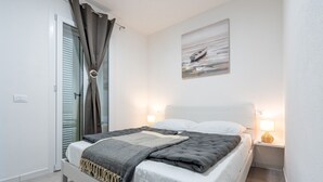 A bedroom with a bed, bedside lamps, a painting on the wall, and a door with curtains. - Affittimoderni Castelsardo - White Breeze (Castelsardo)