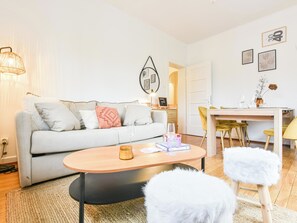 A modern living room with a sofa, coffee table, and a dining area with chairs and a table. - Rock in Share - Bianca – 2-Bedroom Apartment with Parking Included & Tram (Strasbourg)