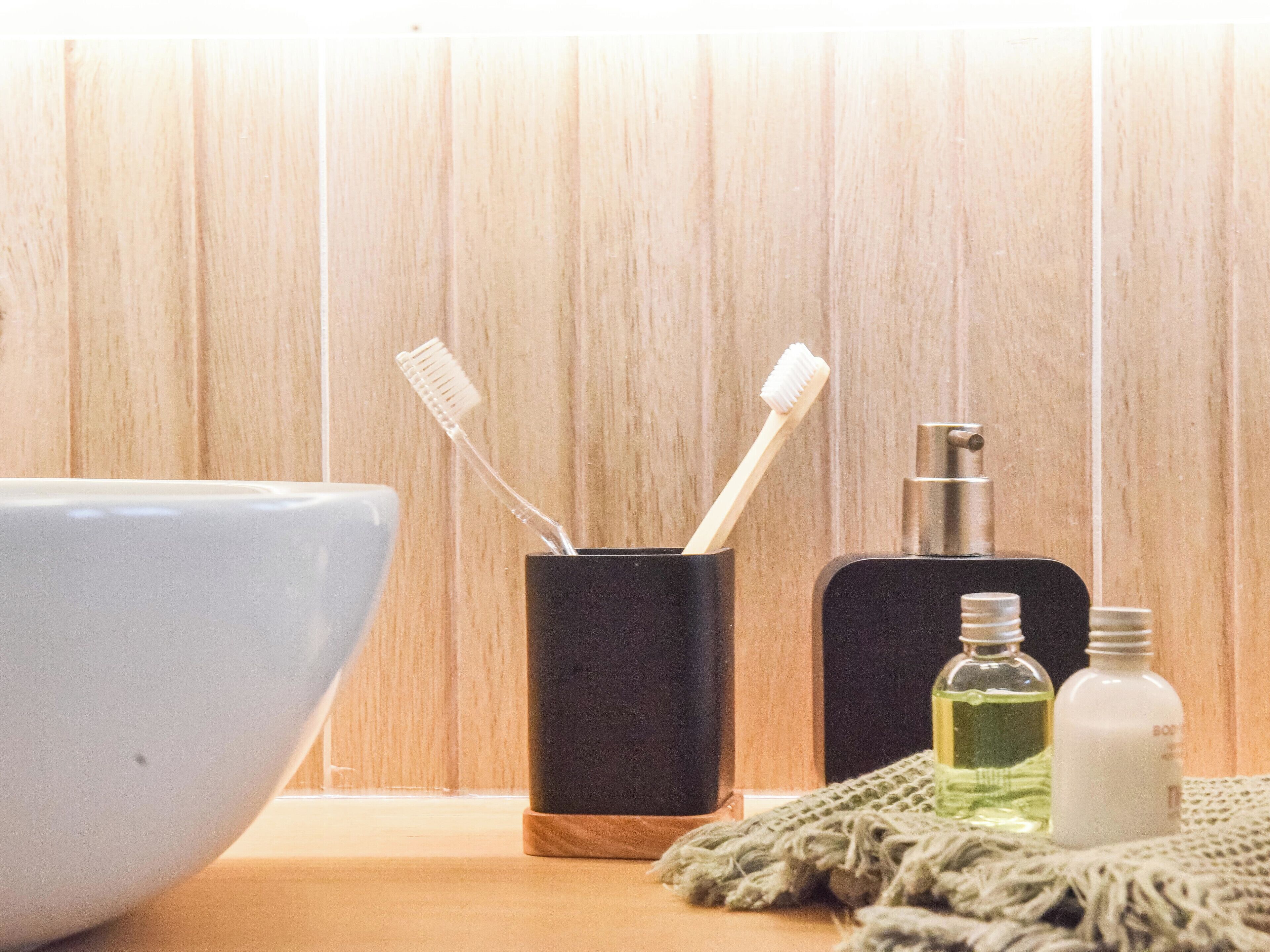 Une salle de bain avec un mur en bois, un lavabo blanc, un porte-brosse à dents noir, un distributeur de savon noir et une bouteille de savon liquide.
