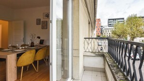 A balcony with a metal railing, a dining area with a table and chairs, and a view of the street and buildings. - Rock in Share - Bianca – 2-Bedroom Apartment with Parking Included & Tram (Strasbourg)